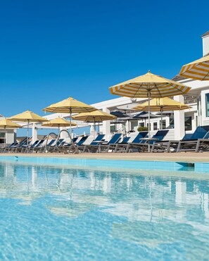 A pool with lounge chairs and striped umbrellas. - Crabby Patty: Pool Access | Short Walk to Beach (Nags Head)