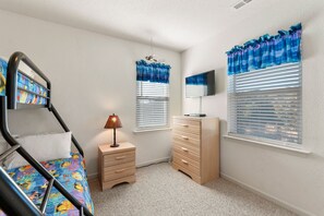 A bedroom with a bunk bed, a dresser, a lamp, and two windows with blue curtains. - Crabby Patty: Pool Access | Short Walk to Beach (Nags Head)