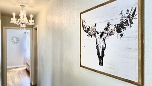 Un pasillo con un candelabro, una obra de arte floral en blanco y negro enmarcada en la pared, y una alfombra estampada en el suelo.