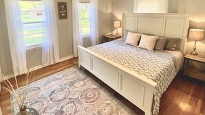Un dormitorio con una cama, dos mesitas de noche, un ventilador de techo y una ventana con cortinas.