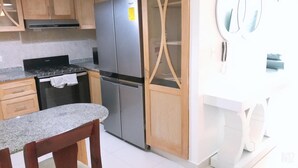 Une cuisine dotée de plans de travail en granit, d’un réfrigérateur en acier inoxydable, d’armoires en bois et d’une chaise en bois.