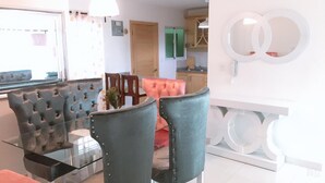 Un espace de repas moderne avec une table en verre et des chaises à capitonnage, une porte en bois et une cuisine en arrière-plan.