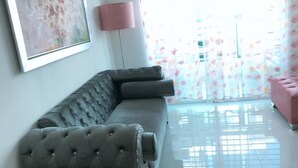 Un salon avec un canapé gris, un pouf rose et une œuvre d’art encadrée accrochée au mur.