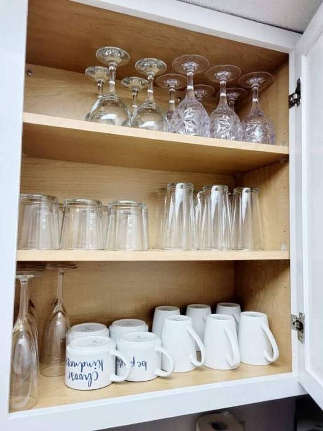 A cabinet with shelves holding various glassware, including wine glasses, tumblers, and mugs.