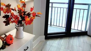 A modern room with a white dresser, a vase of autumn leaves, and a large window with a balcony. - 1510 Pearl on the Beach. Pet Friendly. Oceanfront. (Myrtle Beach)