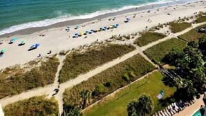 A beach with umbrellas and sun loungers, a clear sky, and a view of the ocean. - 1510 Pearl on the Beach. Pet Friendly. Oceanfront. (Myrtle Beach)