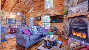 A cozy log cabin interior with a fireplace, leather sofa, and wooden floors.