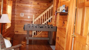 A wooden interior with a foosball table, a staircase, and a lamp.
