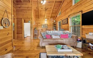 A wooden cabin interior with a sofa, a table, and a window.