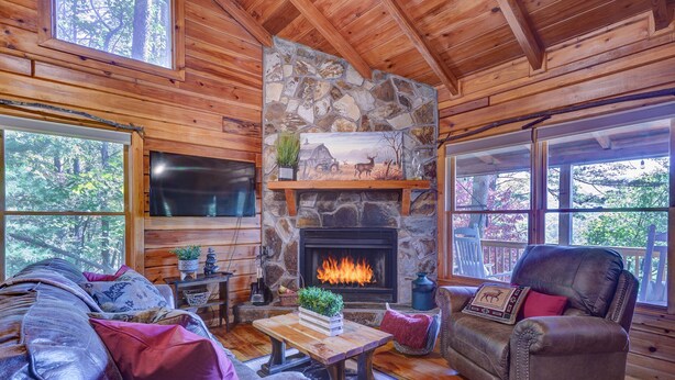 A cozy cabin interior with a stone fireplace, wooden walls, and a leather couch.