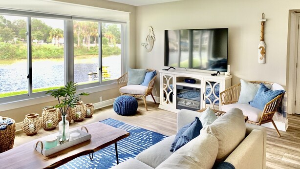 Ein geräumiges Wohnzimmer mit großem Fenster, Deckenventilator, Flachbildfernseher und einer gemütlichen Sitzecke mit Sofa und Sesseln.