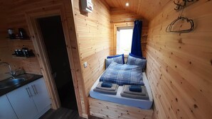 A compact wooden cabin with a kitchenette, a bed with blue bedding, and a window with blue curtains. - Anneth Glamping Pod (Sleat)