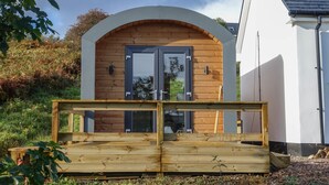 A wooden deck with a bench in front of a building with a white exterior and a sloped roof. - Anneth Glamping Pod (Sleat)