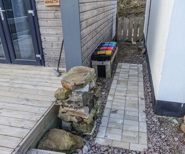 A stone wall with a wooden bench and a small table with colorful items. - Anneth Glamping Pod (Sleat)