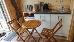 A compact kitchen with a wooden table and chairs, a sink, and a microwave. - Anneth Glamping Pod (Sleat)