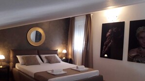 Ett hotellrum med en stor säng, två sängbord, en rund spegel och två inramade tavlor på väggen.
