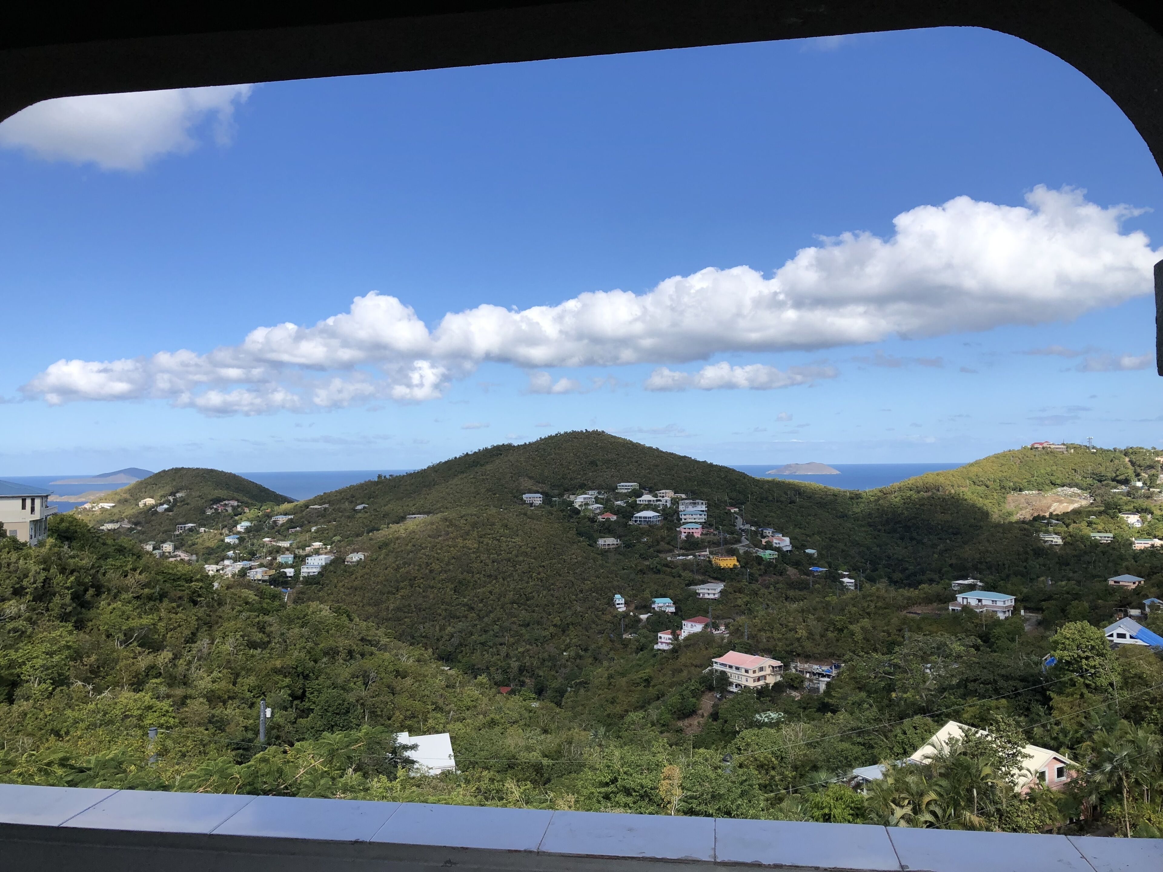 A hillside view with scattered buildings, a clear sky, and distant mountains.