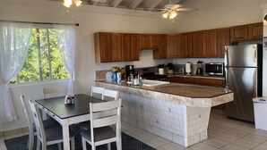 Una cocina con armarios de madera, un refrigerador de acero inoxidable, una encimera de mármol y un comedor con sillas blancas y una mesa.