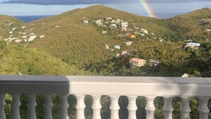Un balcón con vistas a una colina verde exuberante y un arcoíris.
