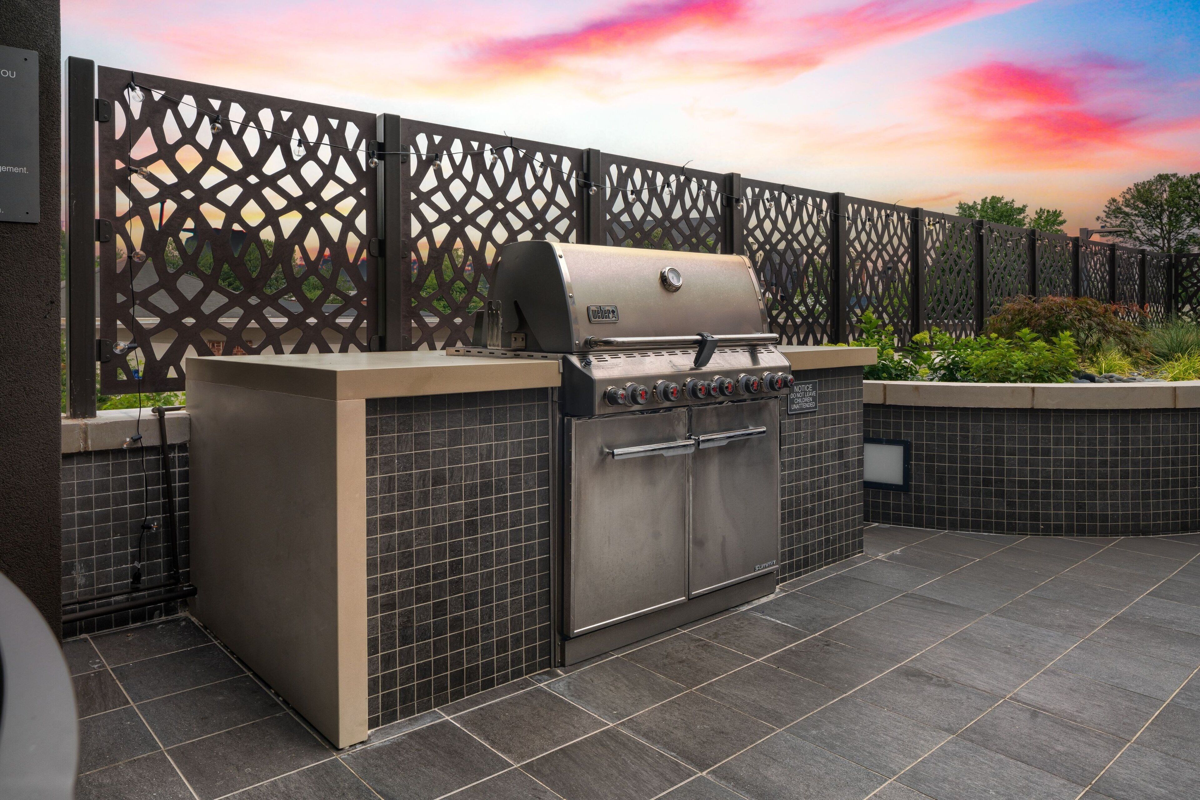 An outdoor kitchen area with a built-in grill, tiled flooring, and a decorative fence.
