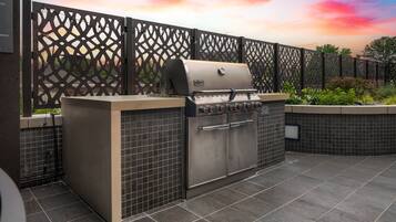 An outdoor kitchen area with a built-in grill, tiled flooring, and a decorative fence.