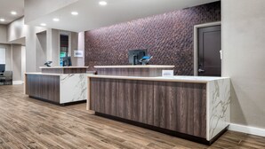 A reception area with two reception desks, a brick-patterned wall, and a wooden floor. - Residence Inn by Marriott Decatur Emory Area (Decatur)