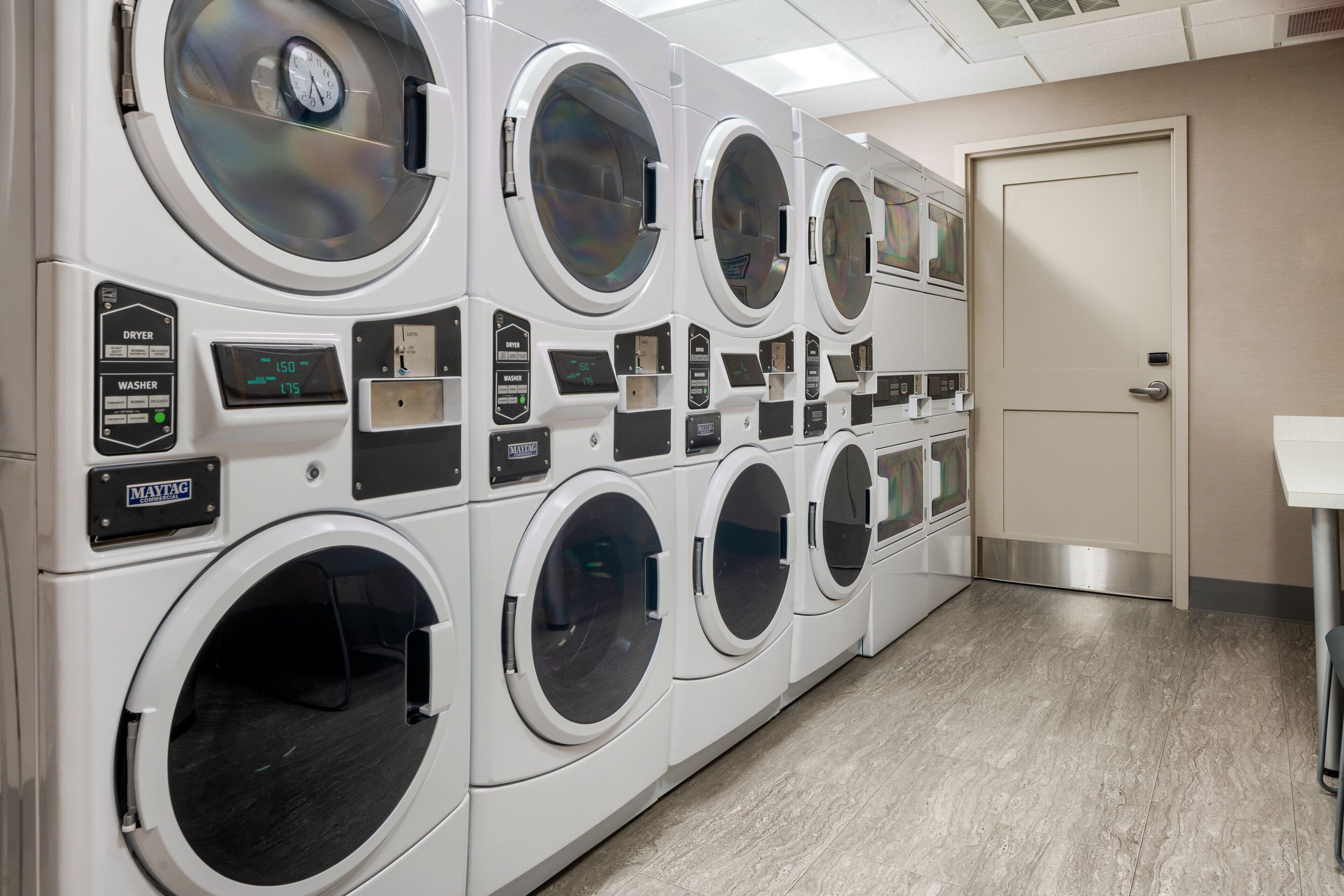 A row of front-loading washing machines in a commercial laundry room with a door and a sink.