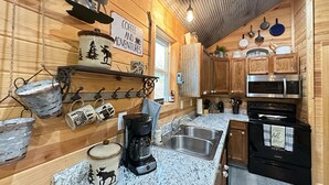 A kitchen with wooden walls, a granite countertop, a coffee maker, a stove, and a sign that says "Coffee and Adventures".
