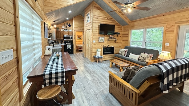 A cozy cabin interior with a wooden interior, a dining area, a living room with a sofa and a TV, and a kitchen with modern appliances.