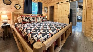 A wooden cabin bedroom with a bed, a ceiling fan, and a window with curtains.