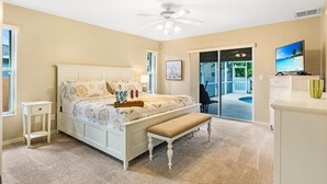 A bedroom with a bed, a bench, a ceiling fan, a TV, and a view of a pool. - Pet-friendly villa w/fenced in yard, bikes & electric heated pool! Villa Royal Ann - SWFL Rentals (Cape Coral)