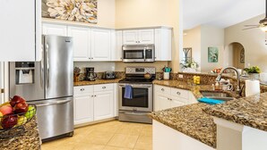 A modern kitchen with white cabinets, stainless steel appliances, granite countertops, and a fruit bowl. - Pet-friendly villa w/fenced in yard, bikes & electric heated pool! Villa Royal Ann - SWFL Rentals (Cape Coral)
