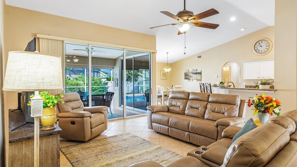 A spacious living room with leather sofas, a ceiling fan, and a view of a pool through glass doors. - Pet-friendly villa w/fenced in yard, bikes & electric heated pool! Villa Royal Ann - SWFL Rentals (Cape Coral)