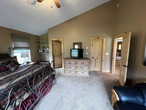 Ein Schlafzimmer mit einem Bett, einem Schminktisch, einem Fernseher und zwei Türen zu anderen Räumen.