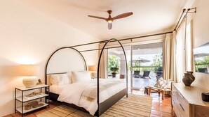 A bedroom with a four-poster bed, a ceiling fan, a nightstand, a dresser, and a view of an outdoor patio. - Peaceful Palmilla Ocean View Oasis Steps to Beach (Palmilla)