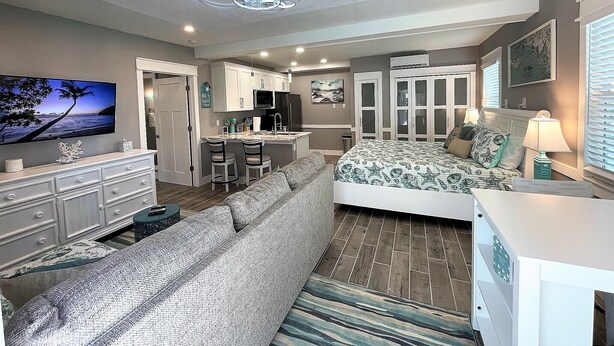 Un dormitorio moderno con una cama grande, un sofá, un televisor y una zona de cocina.