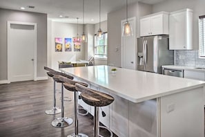 A modern kitchen with white cabinetry, a large island with bar stools, stainless steel appliances, and pendant lighting.