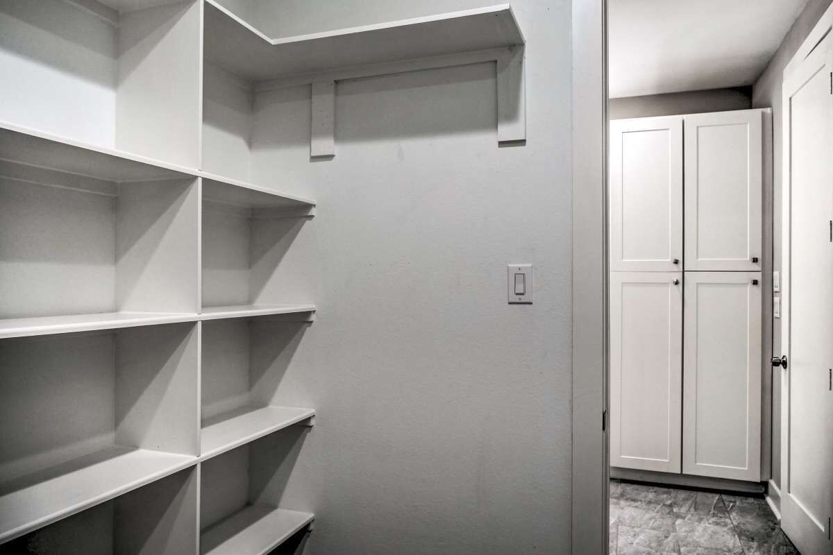 A narrow hallway with white shelving units on one side and a white door on the other.