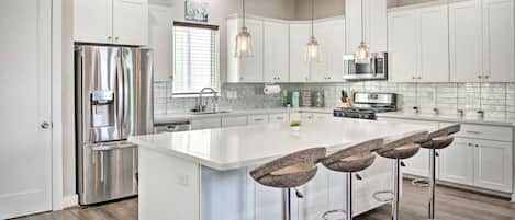 A modern kitchen with white cabinetry, stainless steel appliances, and a central island with bar stools.