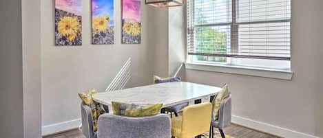 Un comedor con una mesa y sillas, una ventana con persianas y tres cuadros colgados en la pared.