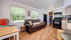Un salón acogedor con un sofá de cuero marrón, suelo de madera y ventanas grandes.