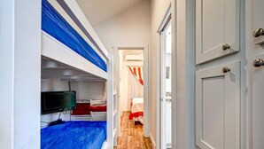 Un pasillo estrecho con literas a un lado y una puerta que da a una habitación con cama y cortinas.