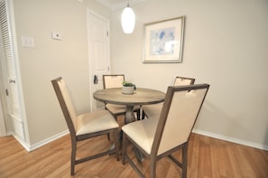 A dining area with a round table, four chairs, a potted plant, and a framed picture on the wall.