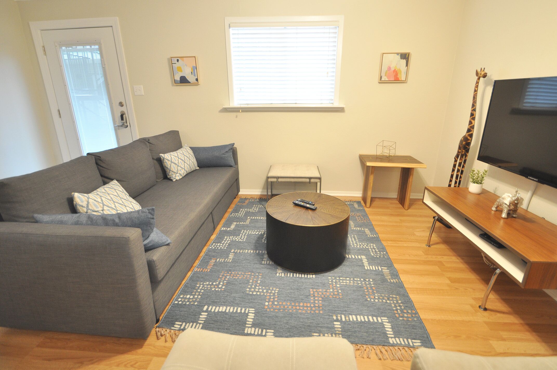 A living room with a grey sofa, a round coffee table, a TV on a wooden stand, and a patterned rug.