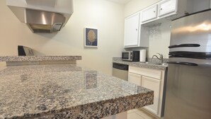 Una cocina con encimeras de granito, electrodomésticos de acero inoxidable, armarios blancos y un microondas.