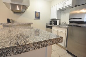 A kitchen with granite countertops, stainless steel appliances, white cabinetry, and a microwave.