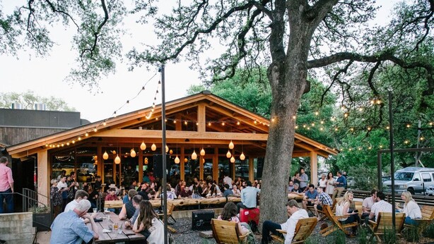 An outdoor dining area with wooden tables and chairs, string lights, and a covered seating area with a wooden roof. - Charming One Bedroom Walkable to Zilker & South Lamar; Secluded multi-unit home (Austin)