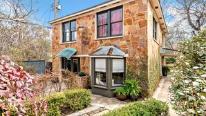 A stone house with a covered porch, a window with a view, and a garden with various plants. - Charming One Bedroom Walkable to Zilker & South Lamar; Secluded multi-unit home (Austin)