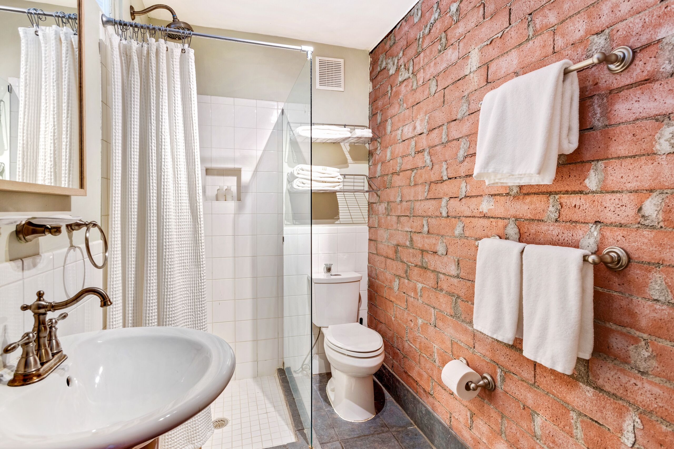 Ein Badezimmer mit einem weißen Waschbecken, einer Toilette, einer Duschkabine aus Glas und einer Ziegelwand.