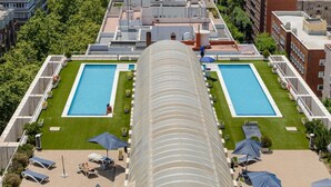 A rooftop swimming pool with two separate sections, surrounded by lounge chairs and umbrellas, and a curved glass canopy overhead. - Charming Eurobuilding Skyline Madrid - Spectacular Views (Madrid)